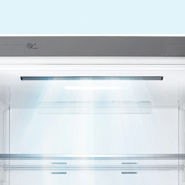 냉장고 내부의 모습입니다. 상단에는 Door Cooling+라는 텍스트가 보이며, 내부 조명이 켜져 있어 밝게 빛나고 있습니다. 냉장고의 내부 선반과 벽면이 보이며, 전체적으로 깔끔하고 현대적인 디자인을 가지고 있습니다.